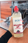 A bottle of eco dishwasher gel unscented held in front of a dishwasher, for an eco-friendly and sustainable home.